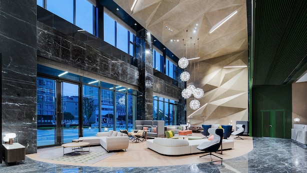 A spacious lobby with a modern design, featuring a large seating area, a high ceiling with geometric patterns, and large windows offering views of the city. - Holiday Inn YONGKANG by IHG (Jinhua)