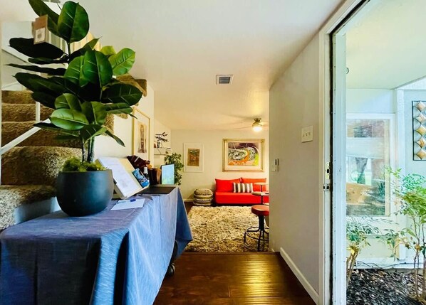 Una sala de estar con una escalera, un sofá rojo, una mesa con mantel azul y una planta grande.