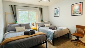 Un dormitorio con dos camas, un ventilador de techo, una ventana con cortinas y una silla.