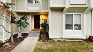 Un edificio residencial de dos plantas con una entrada principal, un pequeño jardín con macetas y una puerta visible.
