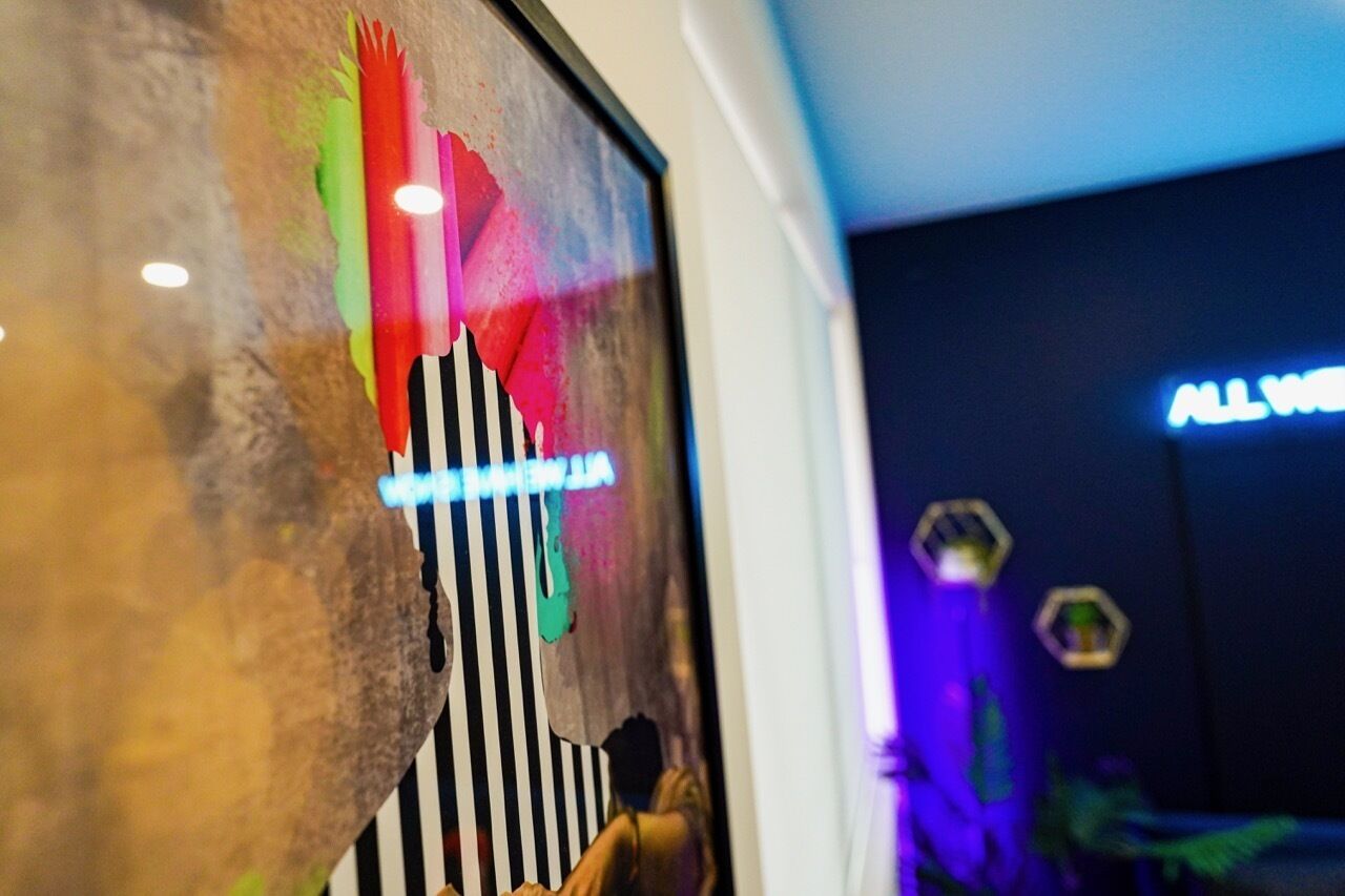 A framed artwork with abstract shapes and a neon sign in the background.