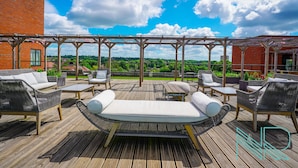 An outdoor patio with wicker furniture, a pergola, and a view of greenery and buildings. - Luxury Stevenage Town Centre Apartment (Stevenage)