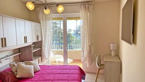 Un dormitorio con cama, escritorio y balcón con sillas.