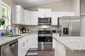 A modern kitchen with white cabinets, stainless steel appliances, granite countertops, and a window with a plant. - Heated Pool Cheerful, Pet- friendly 3 Bedroom (Citrus Springs)