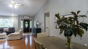 A spacious living room with a dining table, a ceiling fan, and a large plant.