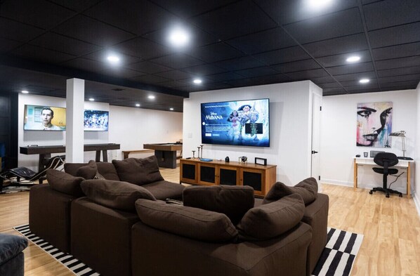 A modern living room with a large brown sectional sofa, a wooden entertainment unit, and a flat-screen TV displaying 'Moana'.