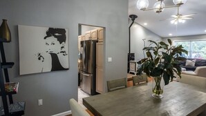 A modern kitchen with stainless steel appliances, a dining area with a wooden table and chairs, and a living room with a sofa and a large window.