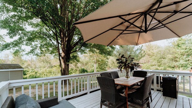 A deck with a table and chairs, a large umbrella, and a tree in the background.