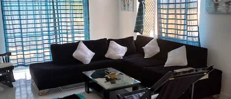 A living room with a black sofa, a glass coffee table, and a black armchair.