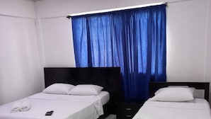A hotel room with two single beds, a nightstand, and a large window with blue curtains.