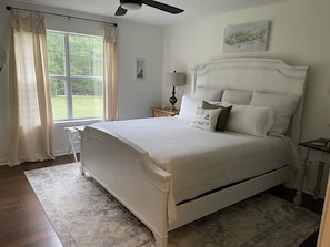 A neatly arranged bedroom with a bed, a bedside table, a lamp, and a window with curtains.