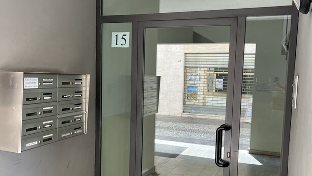 Entrada de un edificio con puerta de vidrio marcada con el número 15, un buzón de correo y un casillero metálico.