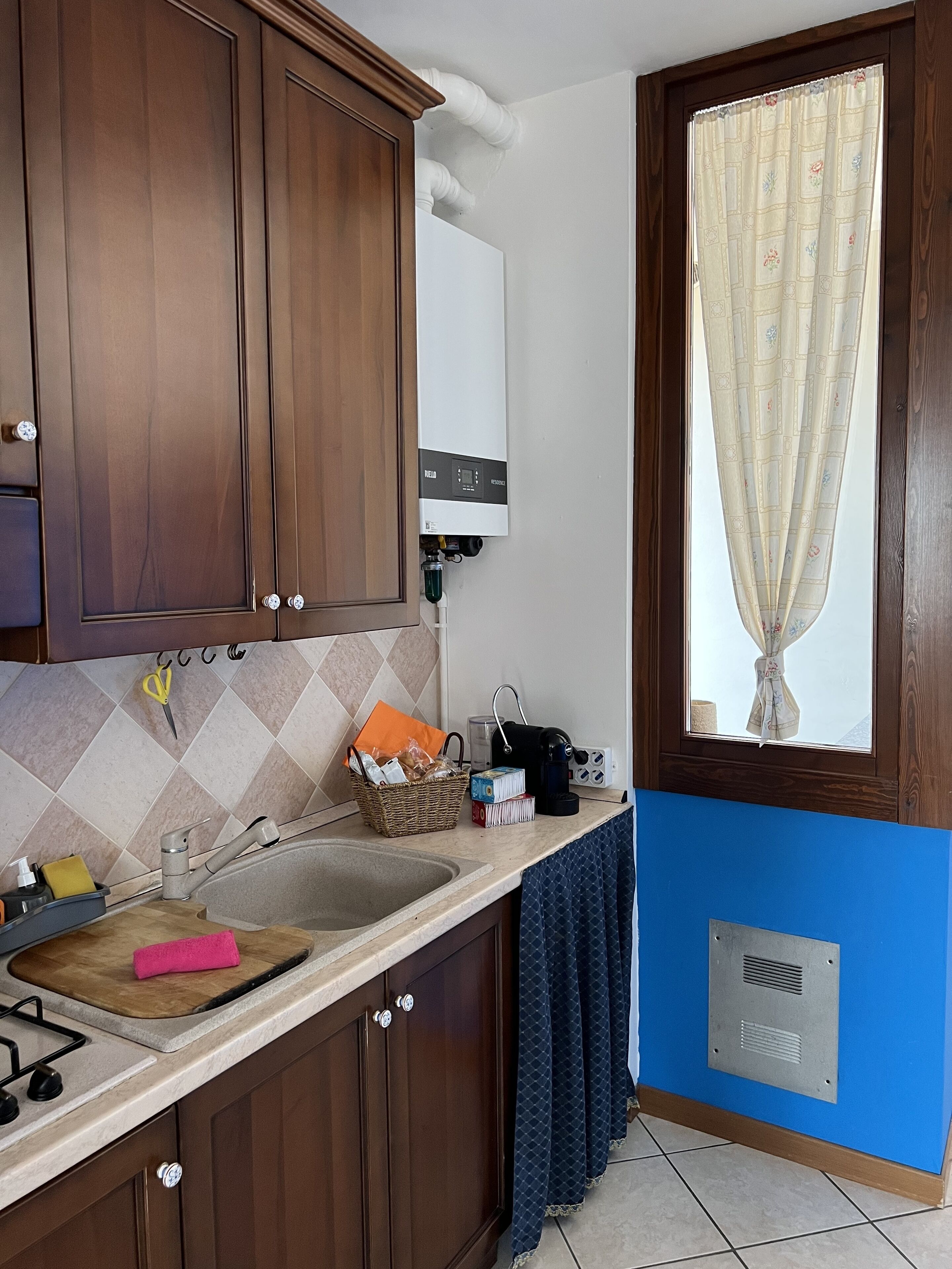 Una cocina con armarios de madera, estufa empotrada, un lavamanos y una ventana con cortina.