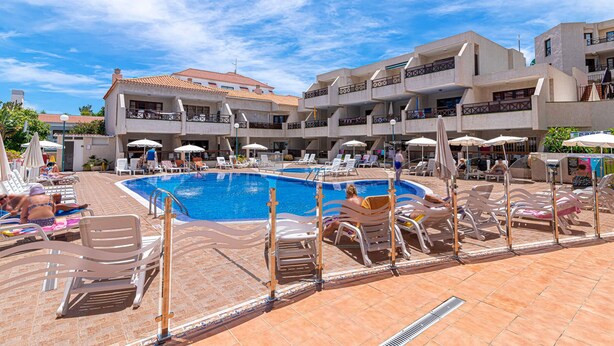 A pool area with sun loungers and umbrellas, surrounded by buildings with balconies. - GO2TENERIFE Apart'Elisa Near the beach & Pool view (Arona)