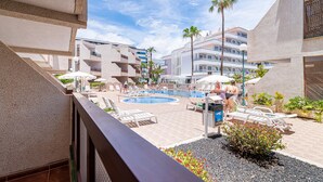 A pool area with lounge chairs and umbrellas, surrounded by buildings with balconies and palm trees. - GO2TENERIFE Apart'Elisa Near the beach & Pool view (Arona)
