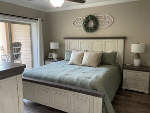 Ein Schlafzimmer mit einem Bett, zwei Nachttischen, einem Deckenventilator, einem Fenster mit Jalousien und einem Sessel.