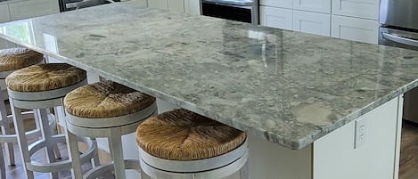 A modern kitchen with white cabinets, a granite countertop, and a central island with stools.