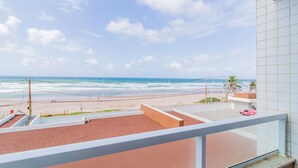 A beach view from a balcony with a clear sky, a sandy beach, and a few palm trees. - PFL01 - Apartamento 2 Quartos -Vista Mar (Salvador)