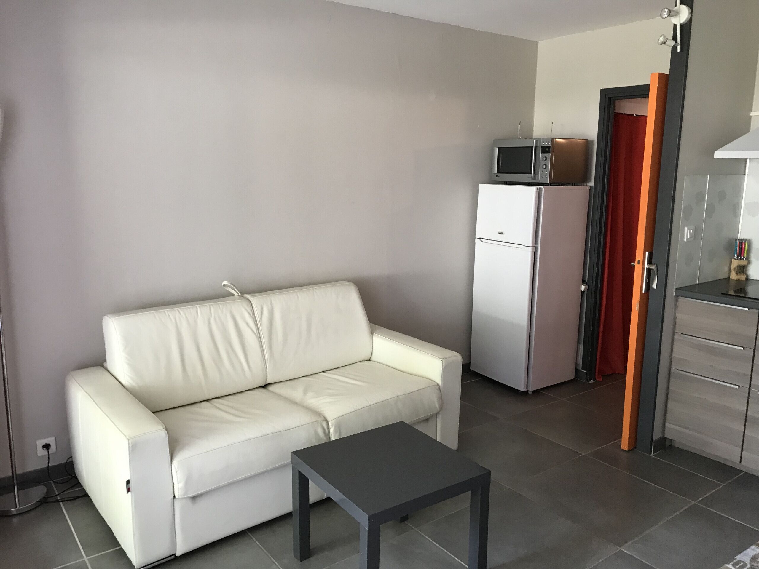 Een moderne woonkamer met een witte bank, een klein zwart tafeltje, een witte koelkast en een magnetron.