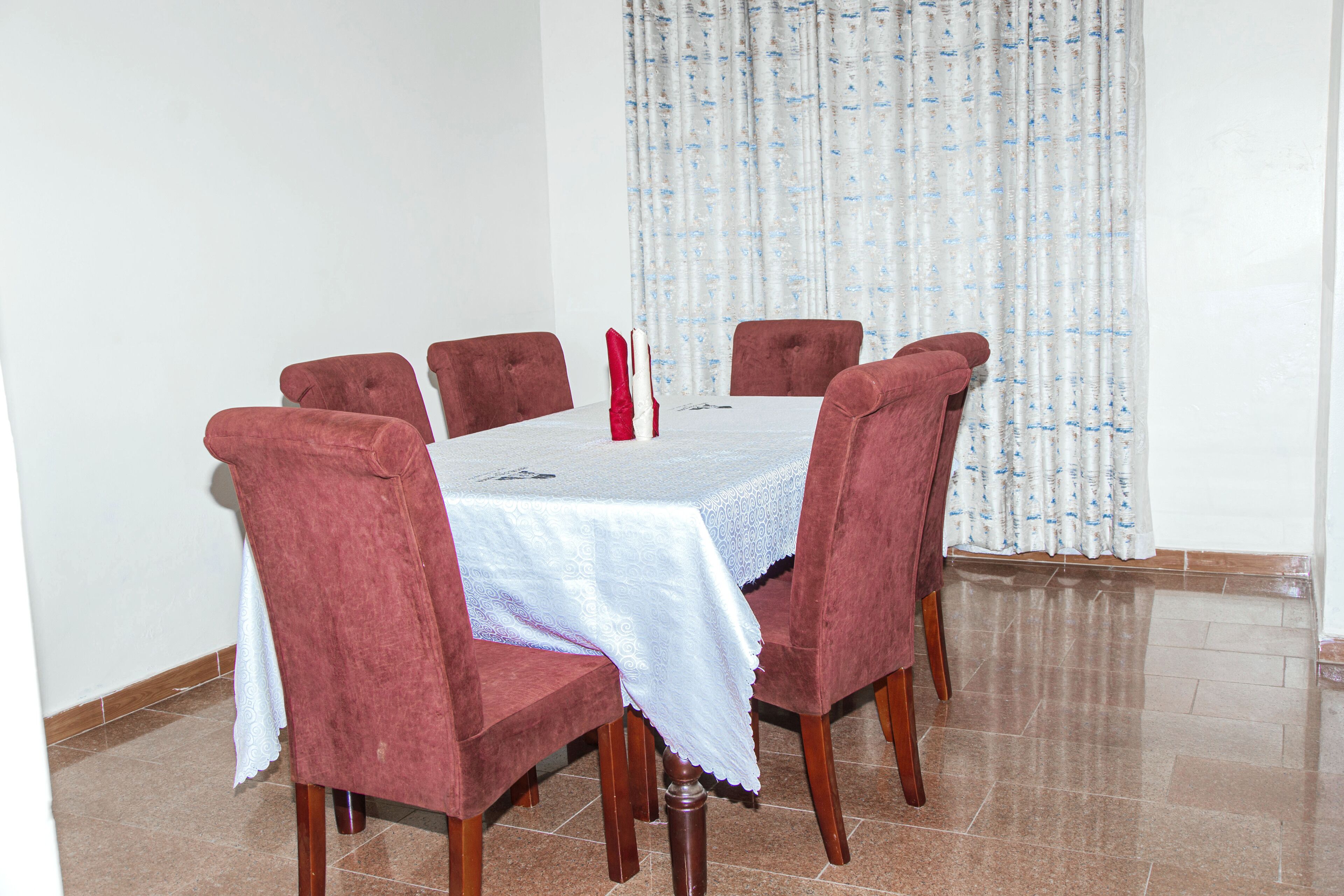A dining area with a round table, six chairs, and a white tablecloth.