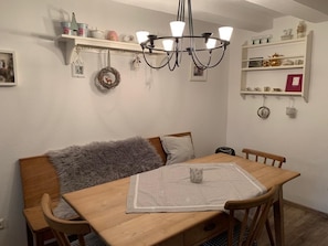 A dining area with a wooden table, chairs, a chandelier, and shelves with decorative items.