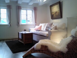 A living room with a sofa, a wicker chair, a small table with a vase, and a painting on the wall.