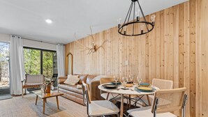 Una habitación acogedora con pared de madera, un sofá de cuero, una mesa de comedor con sillas y un ventanal grande.