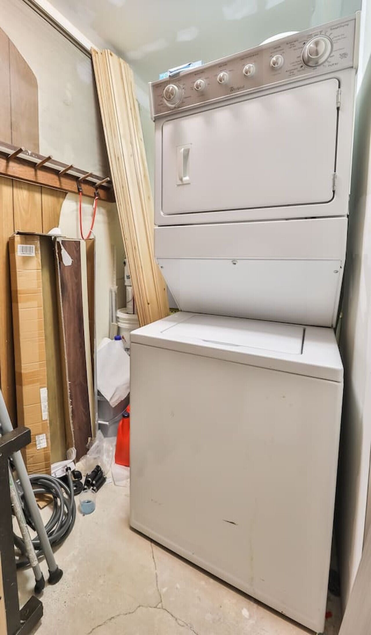 A compact laundry room with a front-loading washer and dryer, wooden cabinets, and a metal rack.