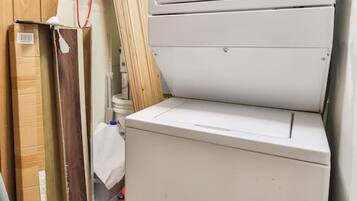 A compact laundry room with a front-loading washer and dryer, wooden cabinets, and a metal rack.