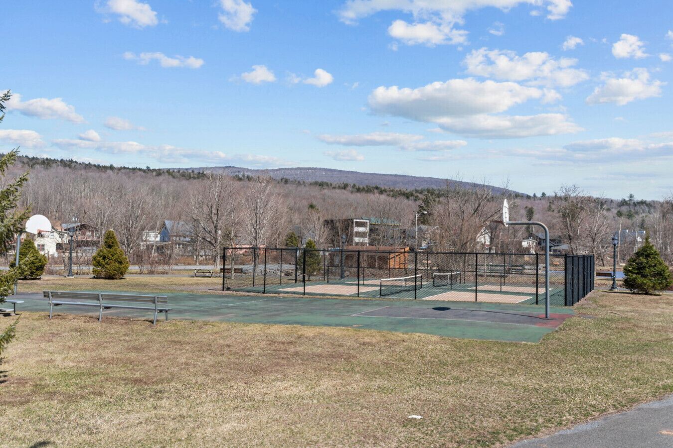 An outdoor park with a basketball court, benches, and a playground area.