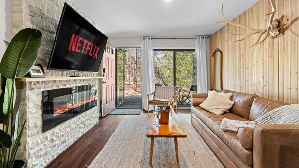 Un salón con chimenea de piedra, sofá de cuero y un televisor montado que muestra 'NETFLIX'.