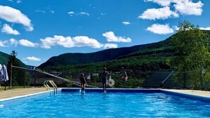 Una piscina con agua azul cristalina, rodeada de una valla y un paisaje montañoso al fondo.