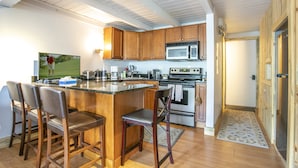 Een keuken met houten kastjes, een magnetron, een oven en een bargedeelte met krukken.