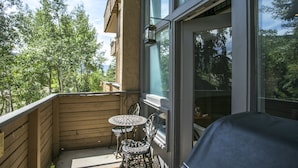 Een houten balkon met een tafel en stoelen, een lantaarn die hangt, en uitzicht op bomen.