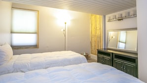 Een slaapkamer met twee bedden, een houten garderobe, een spiegel en een vloerlamp.