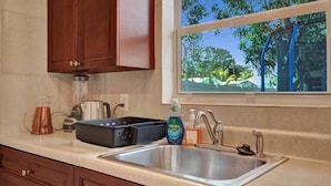 Una cocina con un lavamanos de acero inoxidable, armarios de madera, una cafetera, un hervidor y una ventana con vista a árboles.