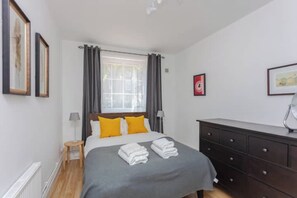 A hotel room with a bed, a bedside table, a dresser, and a window with curtains. - Fantastically Located 2BD Flat in London Bridge (London)