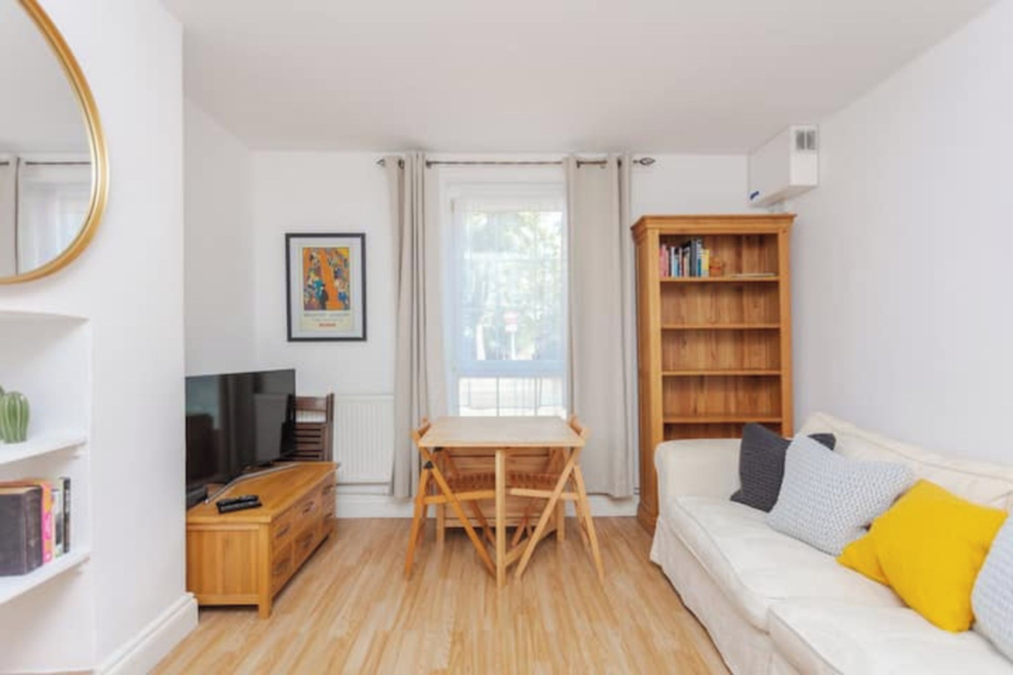 A living room with a sofa, a wooden table, a TV, a bookshelf, and a window with curtains.
