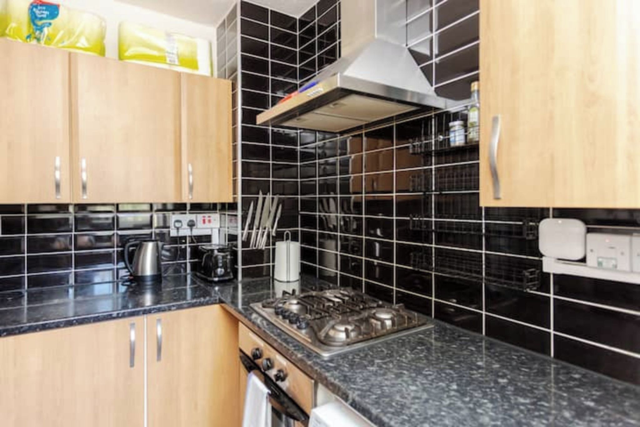 A kitchen with black tiled backsplash, stainless steel appliances, wooden cabinets, and a gas stove.