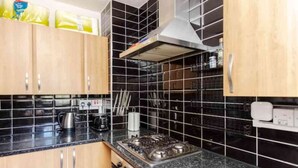 Une cuisine avec des murs recouverts de carreaux noirs, des meubles de cuisine en bois, une cuisinière à gaz et une hotte aspirante.