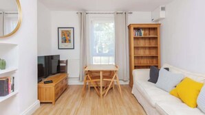 Un salon avec un canapé, une table en bois, un téléviseur, une bibliothèque et une fenêtre.