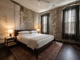 A bedroom with a brick wall, a large bed with white bedding, two bedside lamps, and a window with curtains.