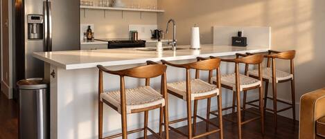 A modern kitchen with a stainless steel refrigerator, a built-in water dispenser, a coffee machine, and a bar area with wooden bar stools.