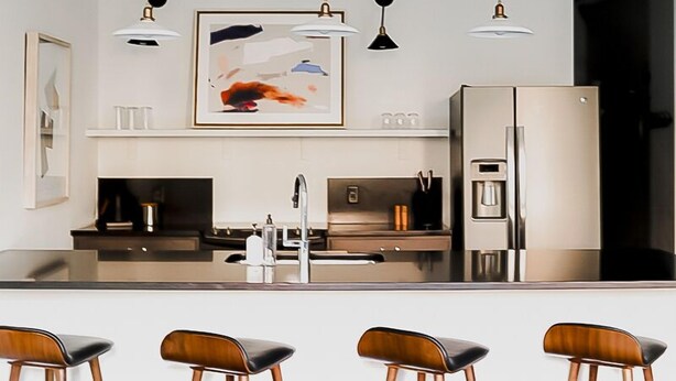 A modern kitchen with a central island, pendant lighting, and bar stools. - The Grant by Black Swan (Savannah)