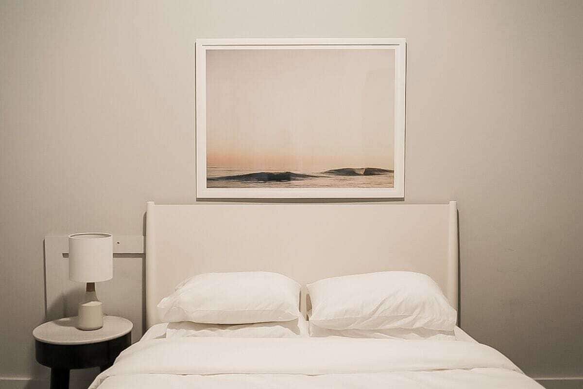 A bed with white bedding, a nightstand with a lamp, and a framed picture above the bed.