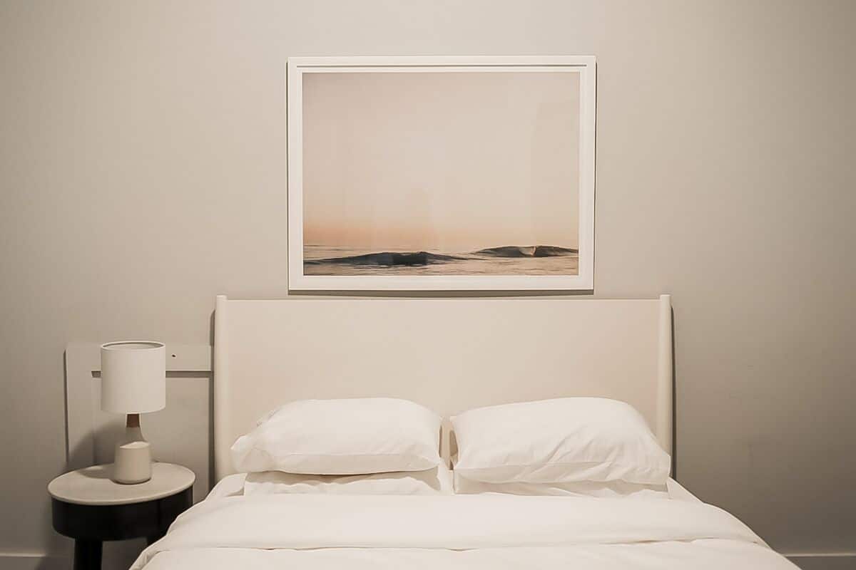 A neatly made bed with white bedding, a bedside lamp, and a framed picture on the wall.