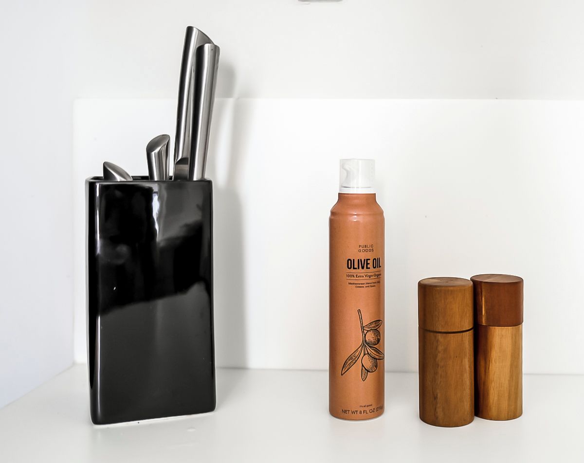 Eine Küchenarbeitsplatte mit einem Messerblock, einer Olivenölflasche und zwei Salz- und Pfefferstreuern aus Holz.