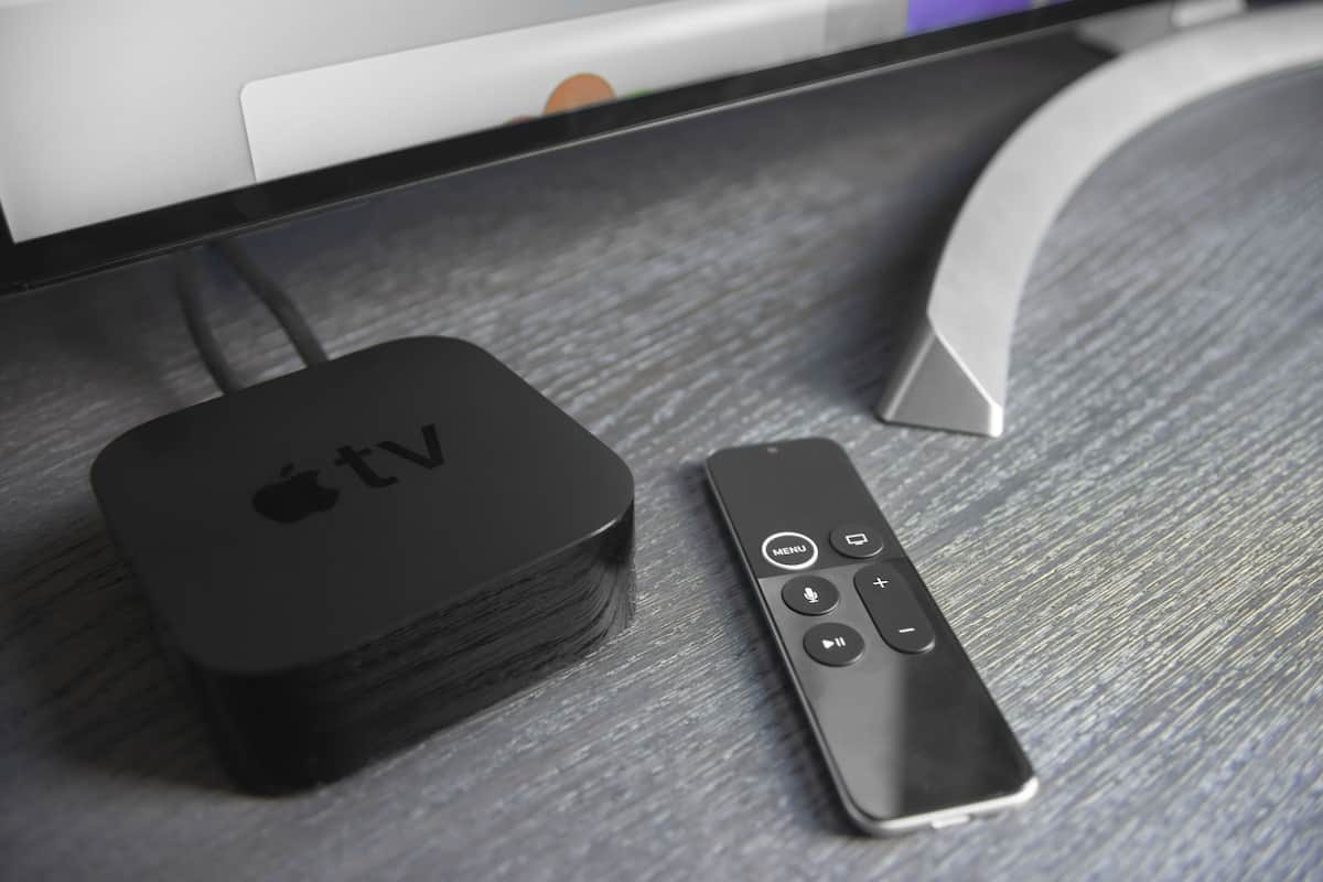 A black Apple TV box and a remote control on a wooden surface.