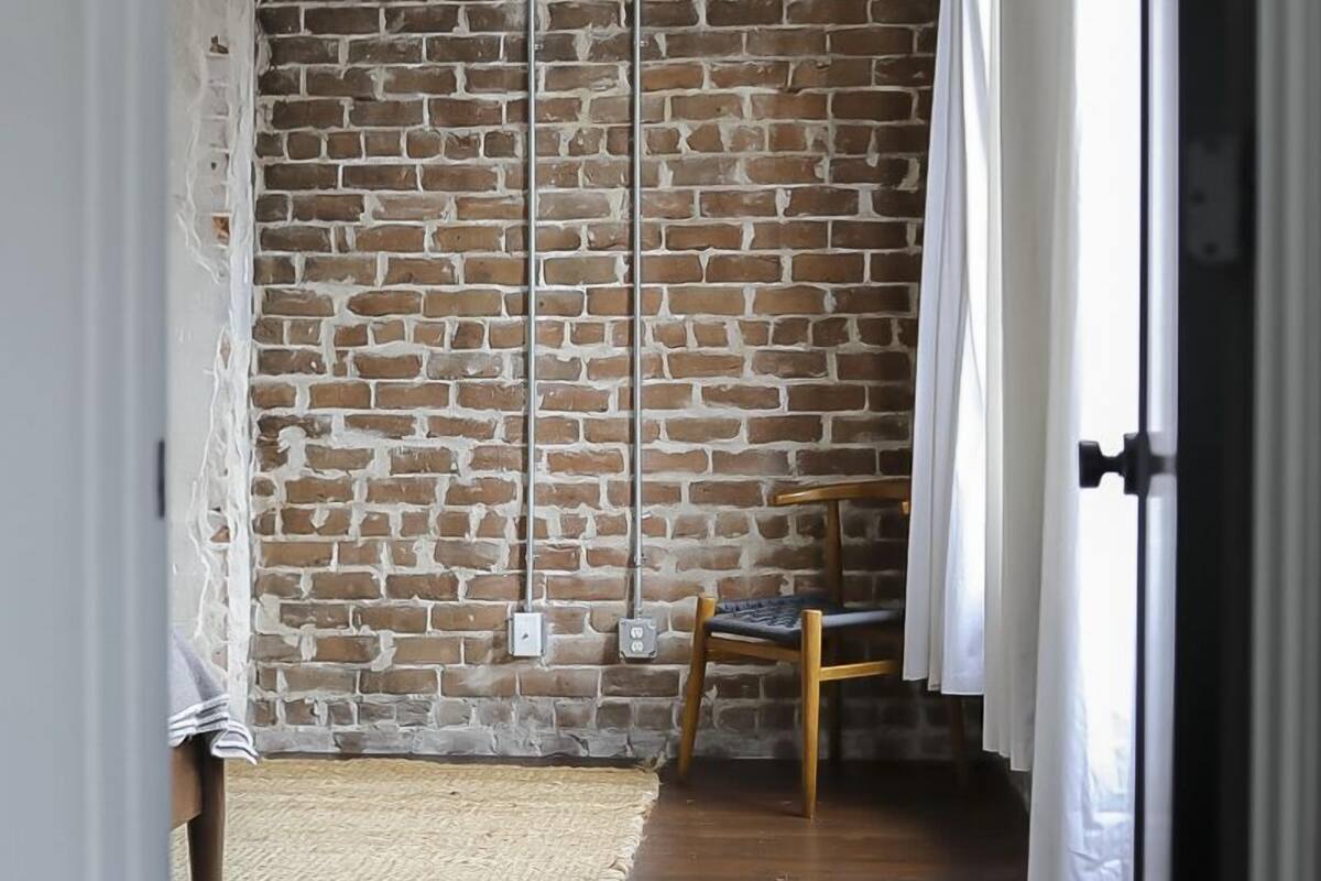 A room with a brick wall, a wooden chair, and a white curtain.