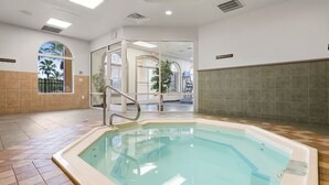 Una piscina con suelo de baldosas, entrada por puerta de cristal y vistas a palmeras al exterior.